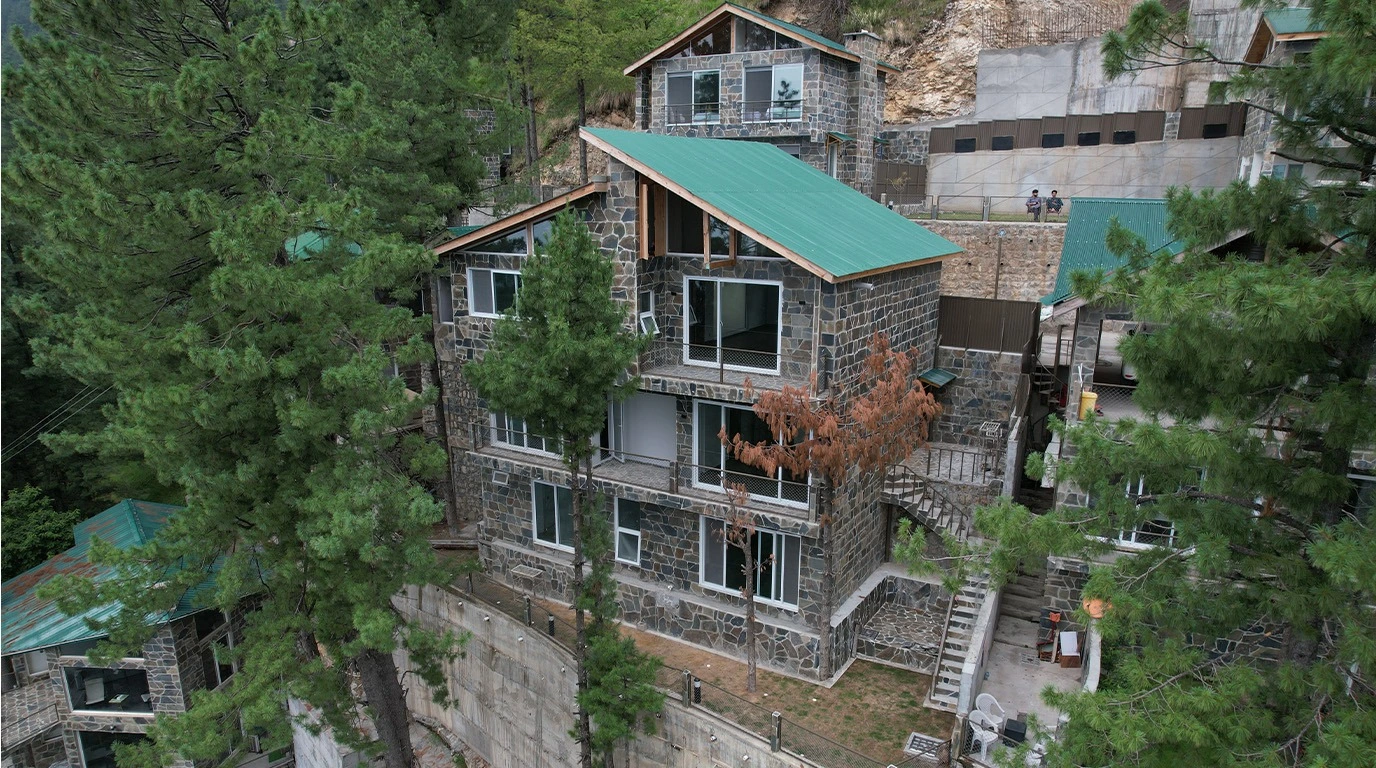 Luxury villa in Galiyat with stone exterior and green roof surrounded by pine trees — Blue Pine Mountain Homes Khaira Gali