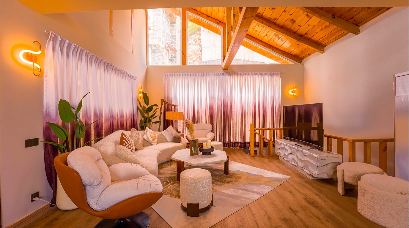 Fully furnished villa living room in Galiyat with vaulted wooden ceiling, designer sofa, and floor-to-ceiling curtains  Blue Pine Mountain Homes