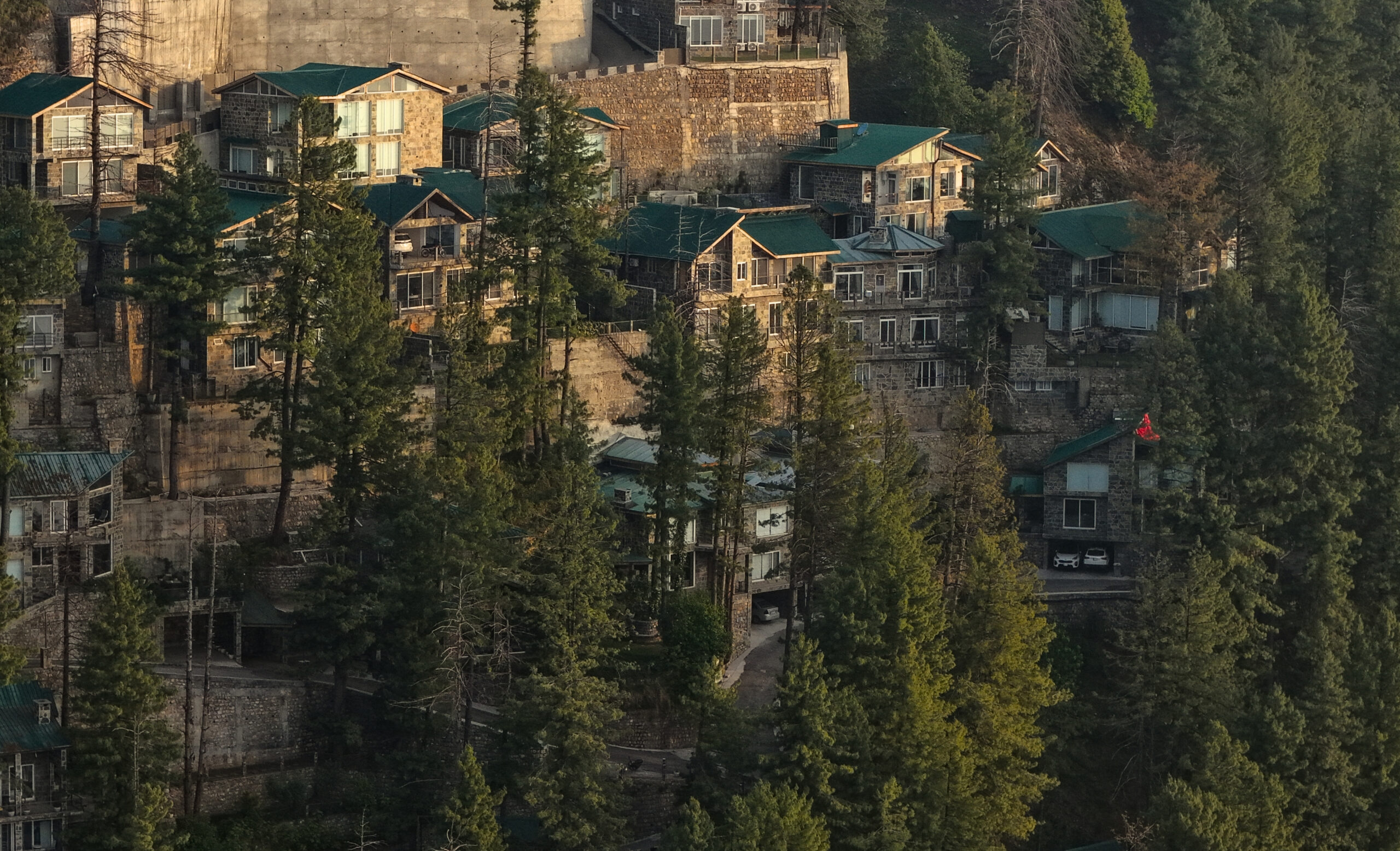 Best real estate investment in Pakistan — aerial view of stone villas with green roofs nestled in pine forest in Galiyat